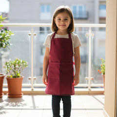 Young girl standing on a balcony wearing a professional burgundy red kids apron with front pocket