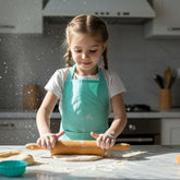 Child wearing a mint green apron using a wooden rolling pin to roll out dough in a kitchen