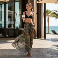 Woman in a peacock print sarong and black bikini top holding a coffee cup outdoors.