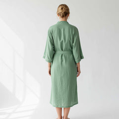 woman wearing a sage green long cotton lounge robe with a waist belt.