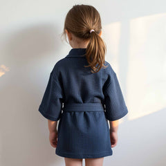 Back view of a little girl wearing a navy blue waffle robe with a belt.