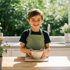 young child in cotton apron holding bowl in outdoor kitchen