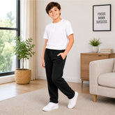 Young boy standing in a living room wearing a white t-shirt, black pants, and white sneakers.