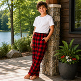 Child wearing red plaid pants and a white shirt standing on a wooden deck by a lake.