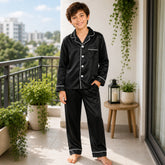 Child wearing black pajamas standing on a balcony with plants and a candle lantern.