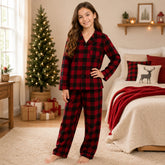Young girl wearing red and black plaid pajamas in a cozy bedroom with a Christmas tree.