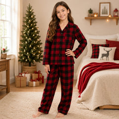 Young girl wearing red and black plaid pajamas in a cozy bedroom with a Christmas tree.