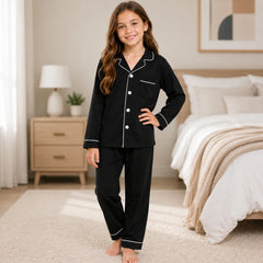 Young girl wearing black pajamas with white trim in a bedroom setting.