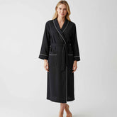 Woman wearing a black full-length robe with white piping and a tie waist.