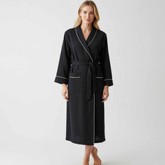 Woman wearing a black full-length robe with white piping and a tie waist.
