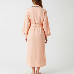 woman wearing a peach cotton long robe with belt and contrast piping.