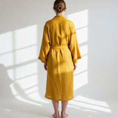 wearing a yellow maslin cotton robe standing in a sunlit room with white walls.