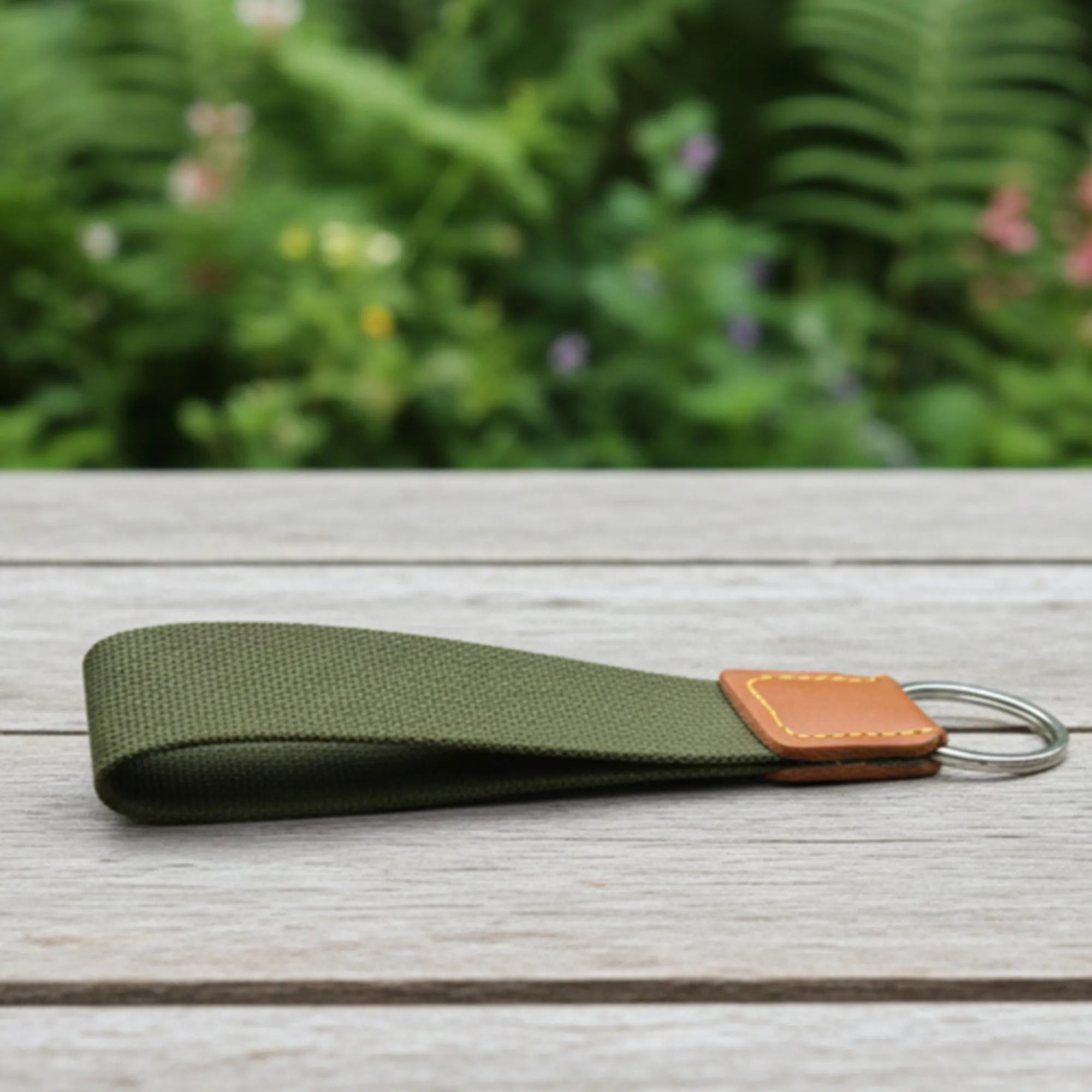 Green keychain with leather tag on a wooden surface with a blurred green background
