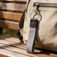 Keychain with gray strap attached to a beige bag on a wooden bench