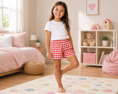 Young boy smiling in a bright blue-themed kids bedroom while wearing blue and white gingham shorts paired with a plain white t-shirt. The gingham shorts feature a clean evenly spaced check pattern, soft lightweight fabric, elastic drawstring waistband, relaxed comfortable fit, and breathable casual styling, photographed with modern bedroom décor, bookshelves, globe décor, soft bedding, and natural sunlight
