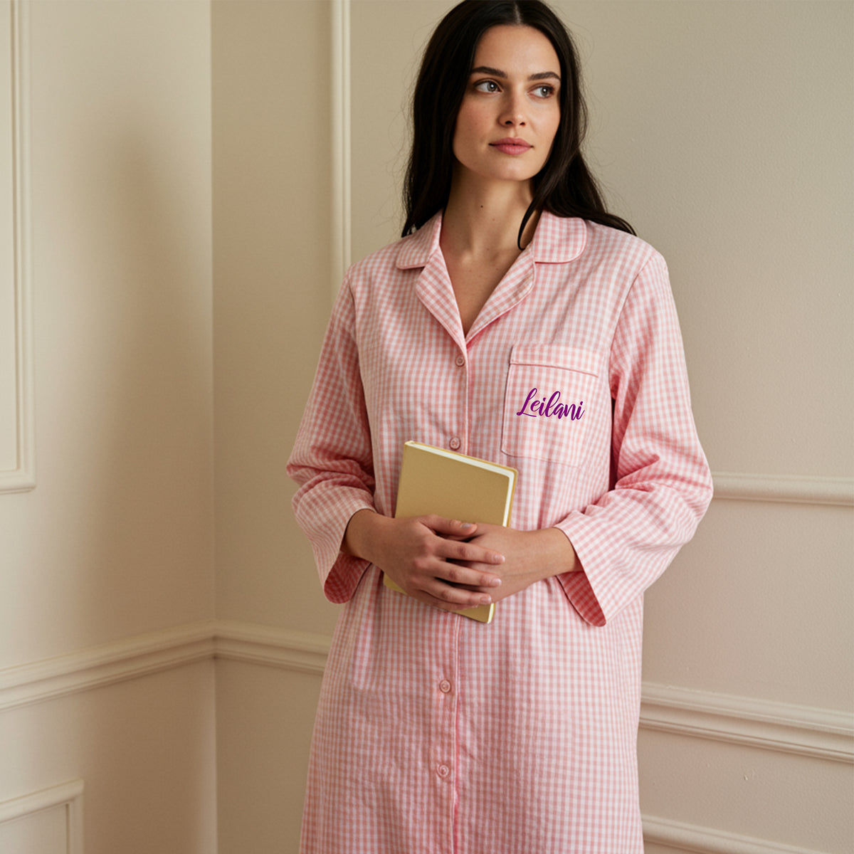 Woman holding a book wearing a pink gingham sleepshirt with purple Leilani embroidery