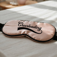 Pink sleep mask with 'Cheerleading' text on a white surface