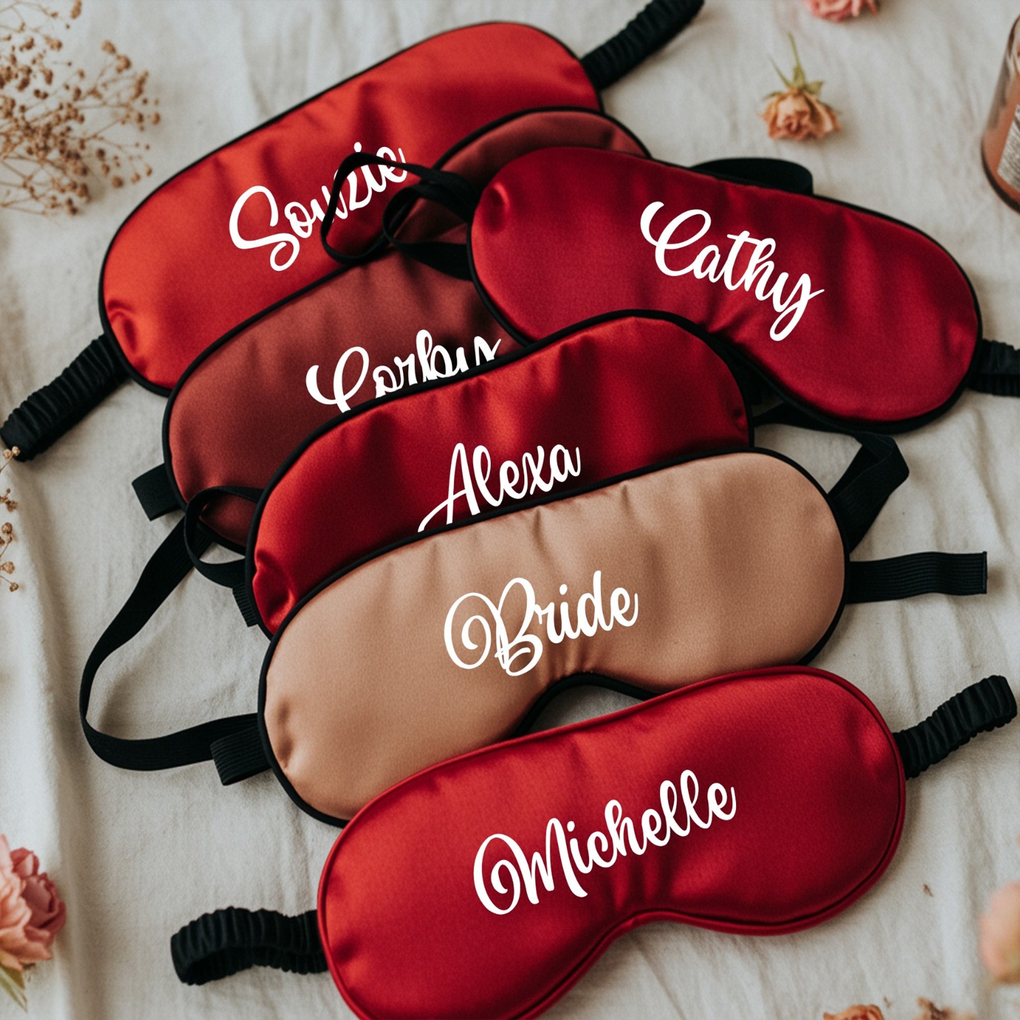 Set of personalized red and brown sleep masks with names embroidered on them, placed on a textured surface.