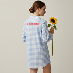 Back view of blue gingham sleepshirt with red Team Bride embroidery holding a sunflower