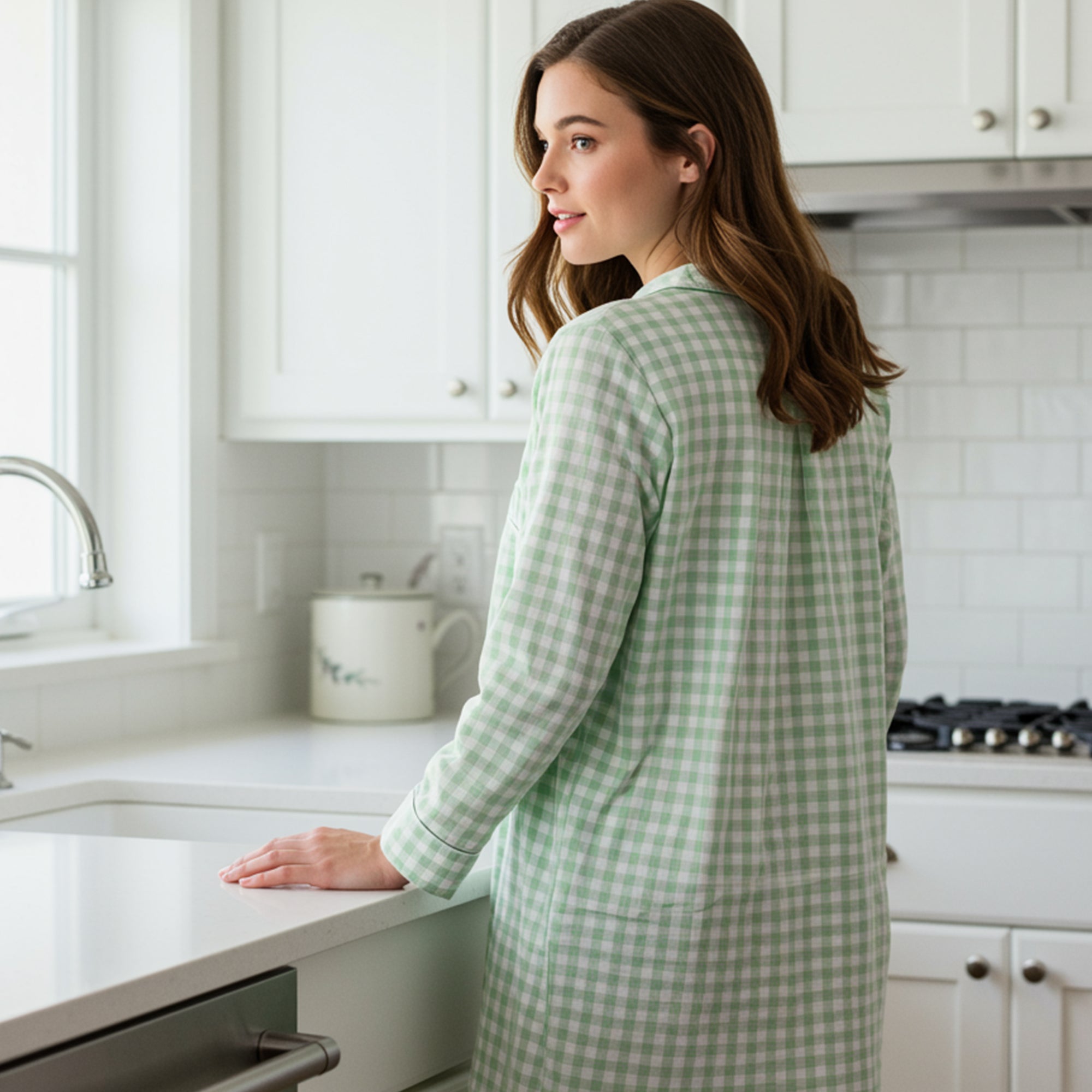 Side profile of a woman in a green gingham cotton nightshirt in a white modern kitchen