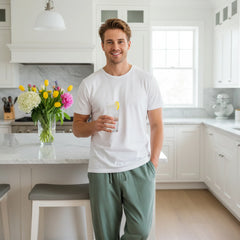 Man holding a glass of lemonade in a modern kitchen with flowers on the counter.