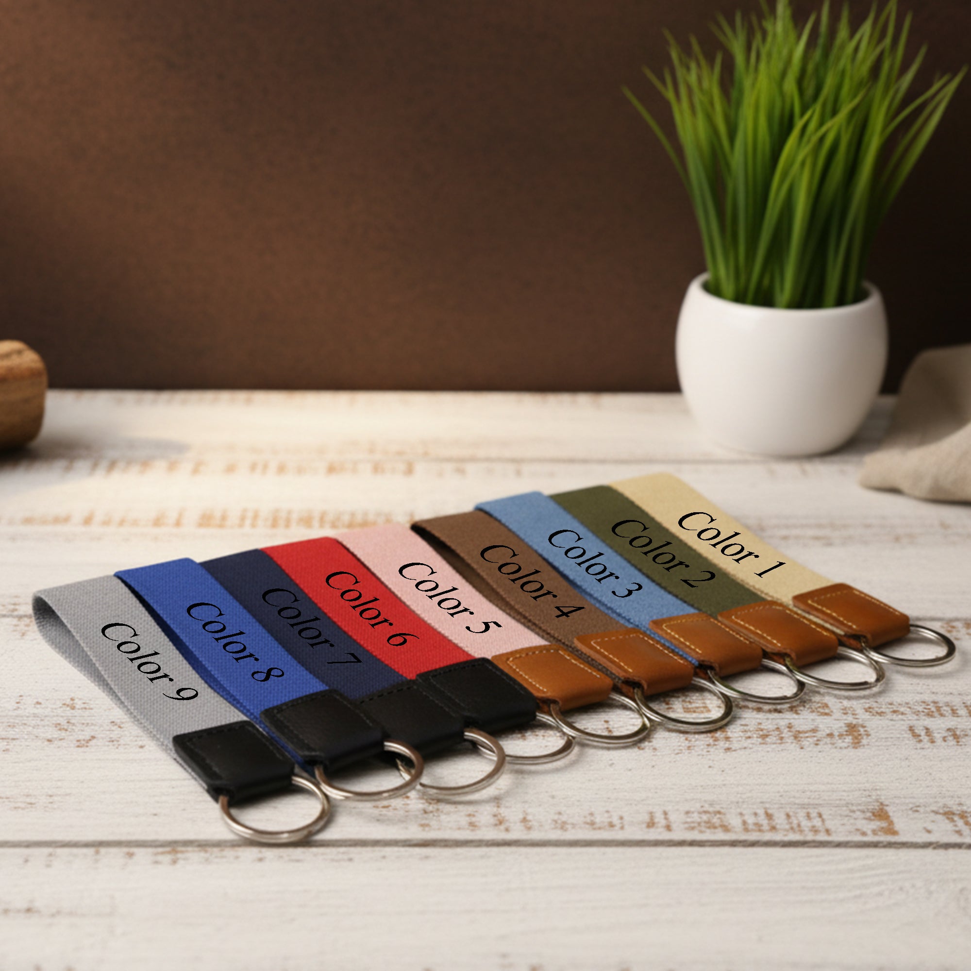 Set of keychains in various colors on a wooden surface with a plant in the background.