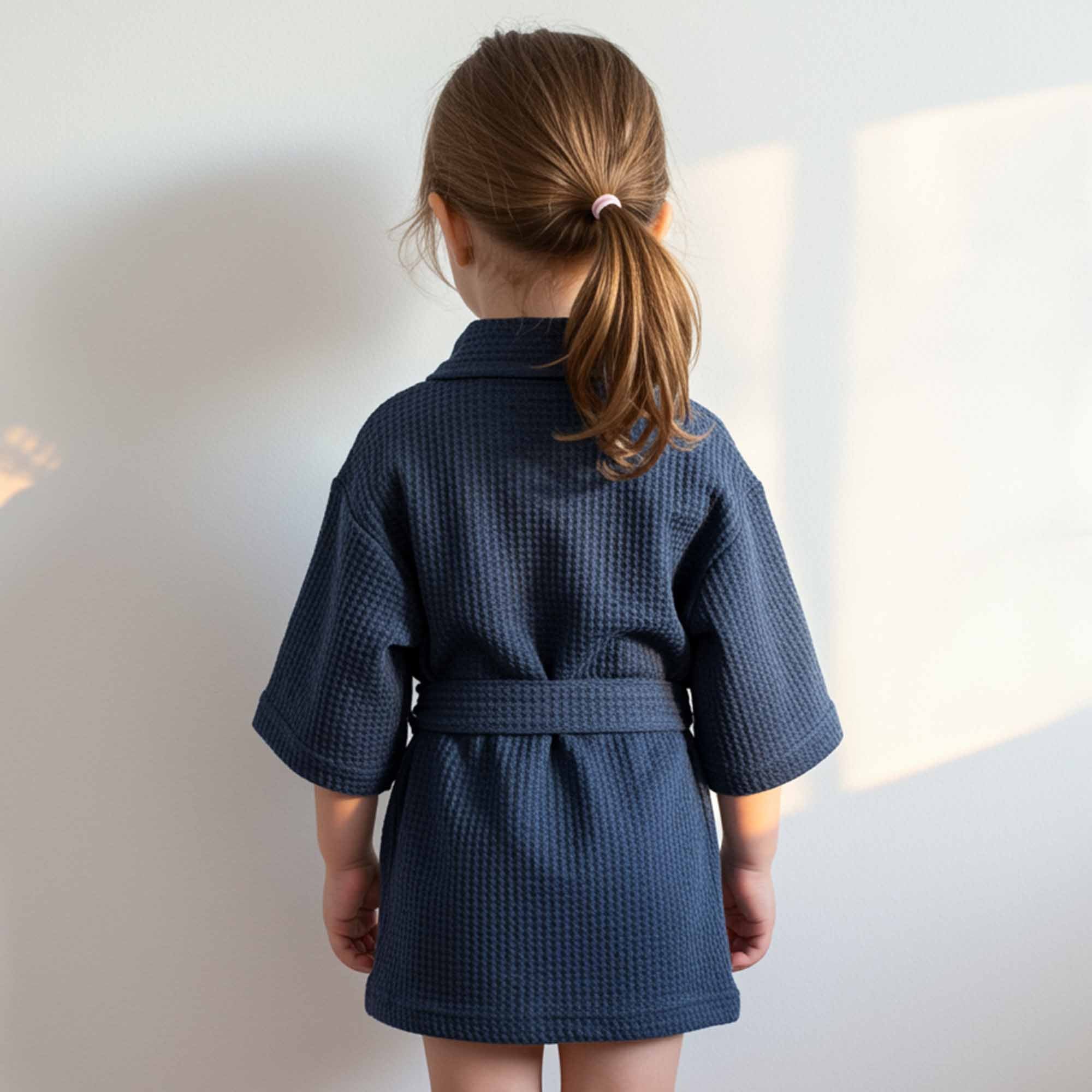 Back view of a little girl wearing a navy blue waffle robe with a belt.