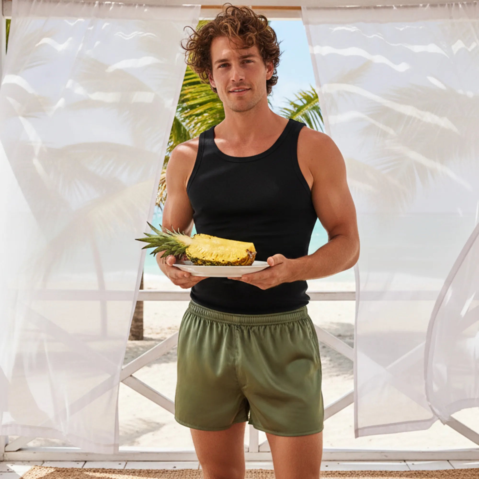 Man holding a pineapple in front of a beach setting