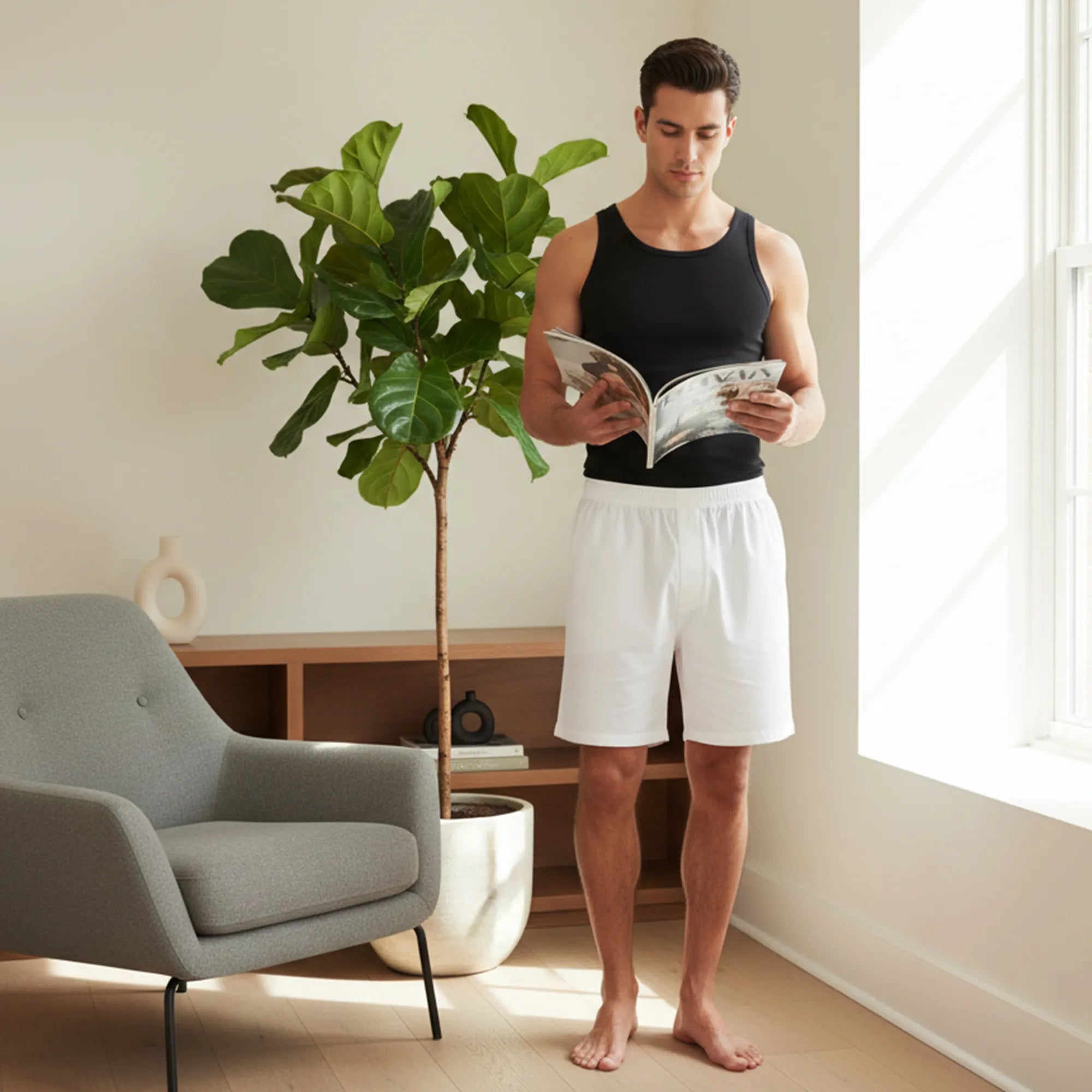 Man reading a magazine in a living room with a plant and chair.
