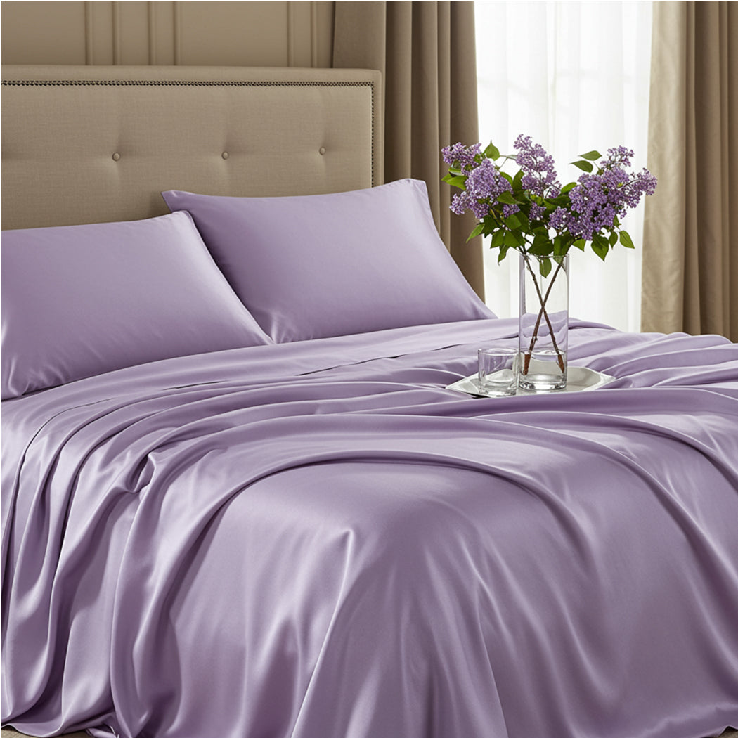 Full view of a rose blush satin bedsheet set with a gold tray and flowers on a cream headboard bed