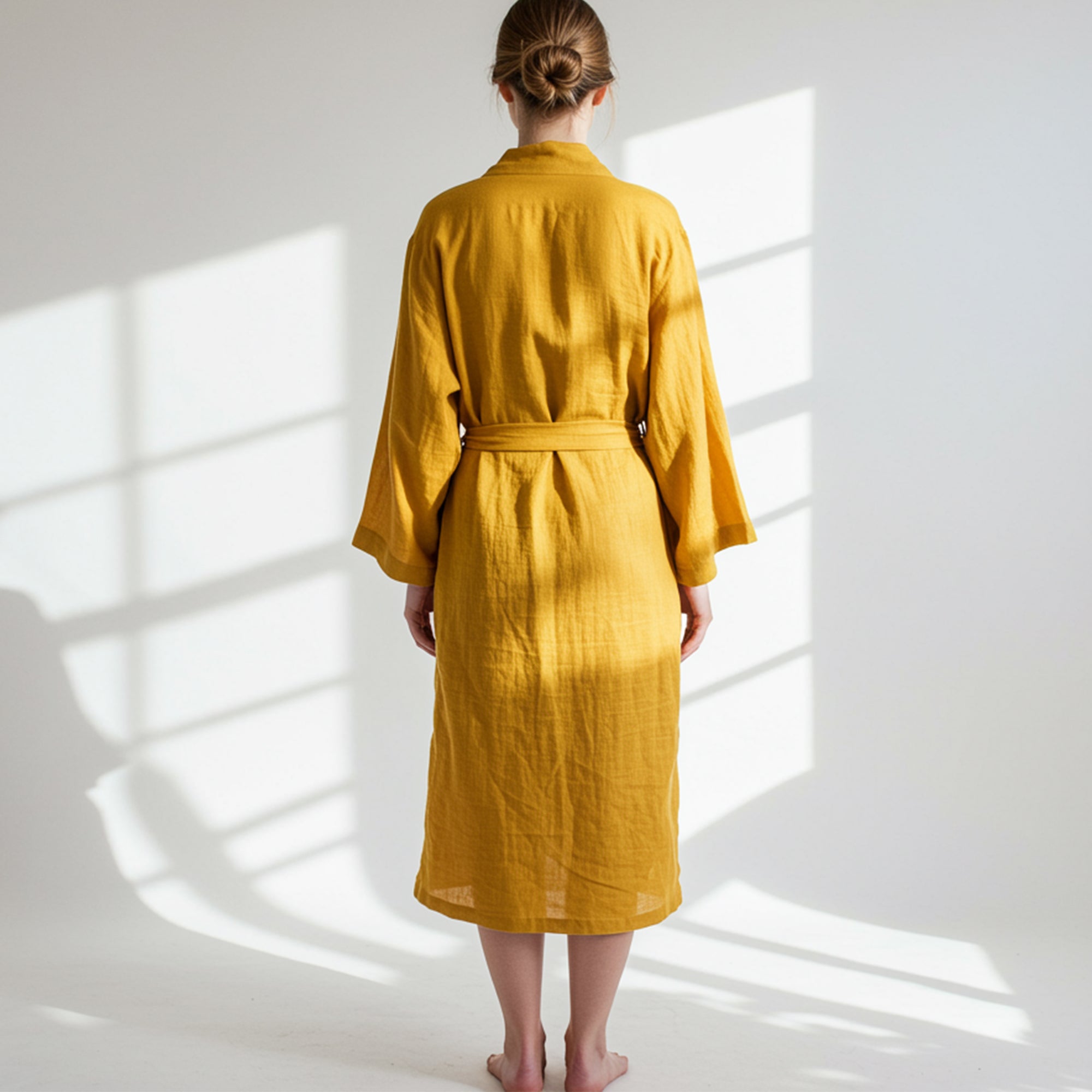 wearing a yellow maslin  cotton robe standing in a sunlit room with white walls.